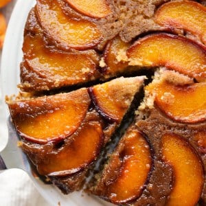 Cutting out a triangular slice of peach upside down cake from the whole cake