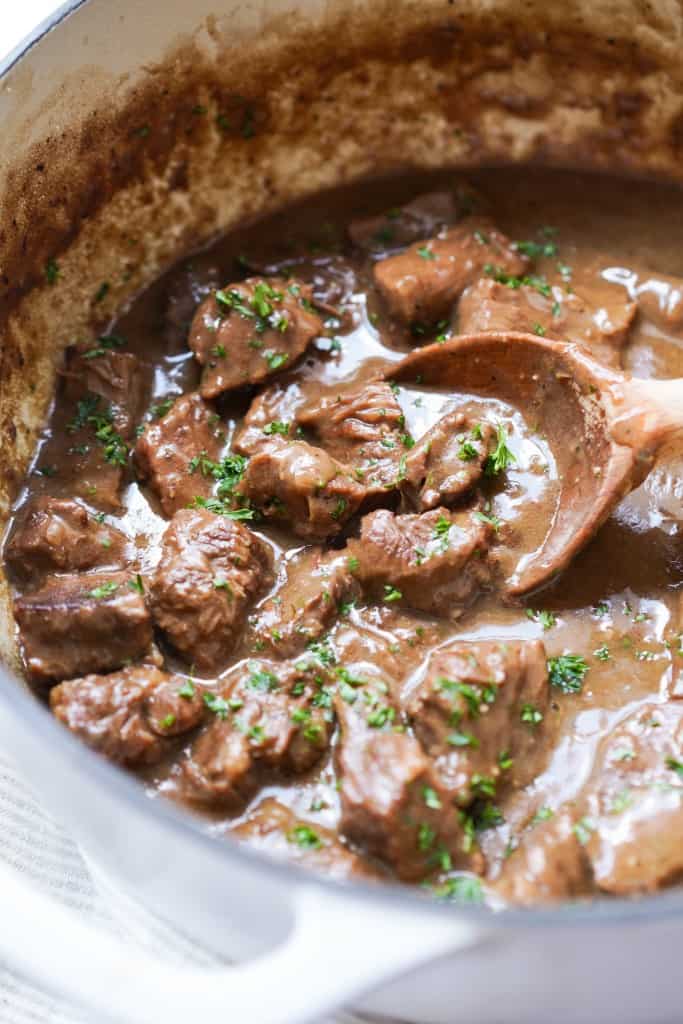 A wooden spoon scooping up beef tips with thick gravy in a pot