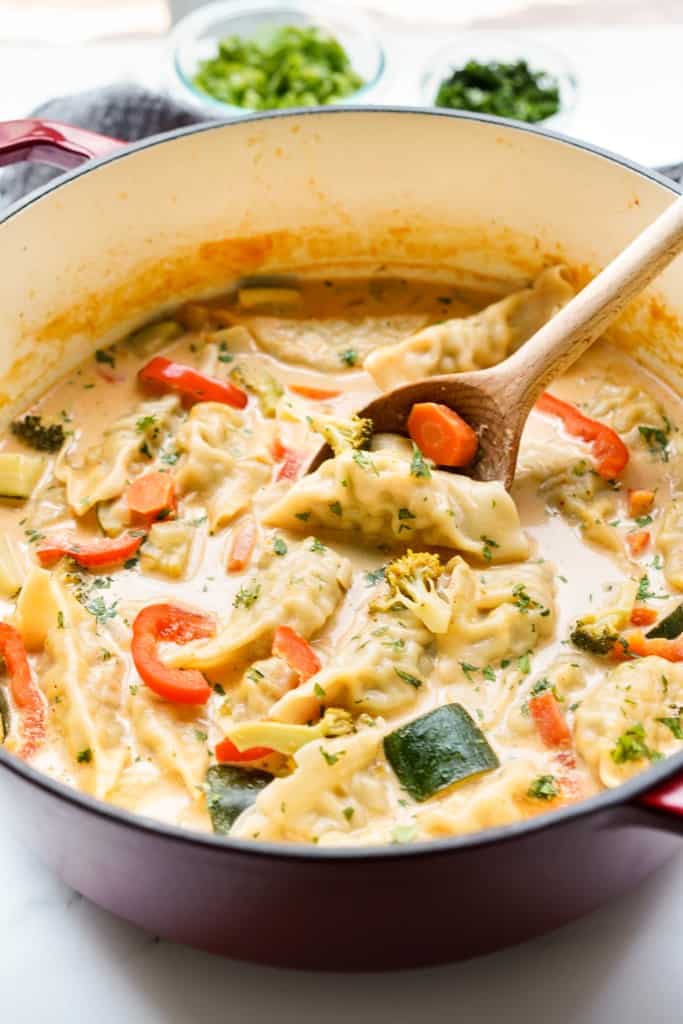 A pot of creamy coconut red curry soup loaded with dumpling, carrot, zucchini and red bell pepper.