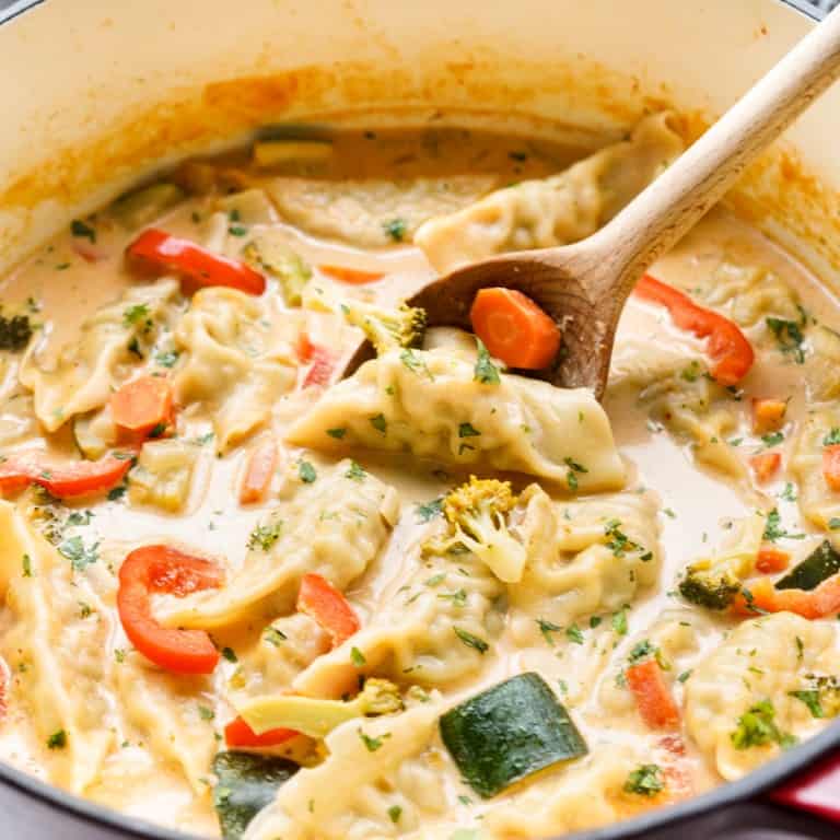 Using a wooden spoon to scoop up a dumpling from a pot of red curry dumpling soup