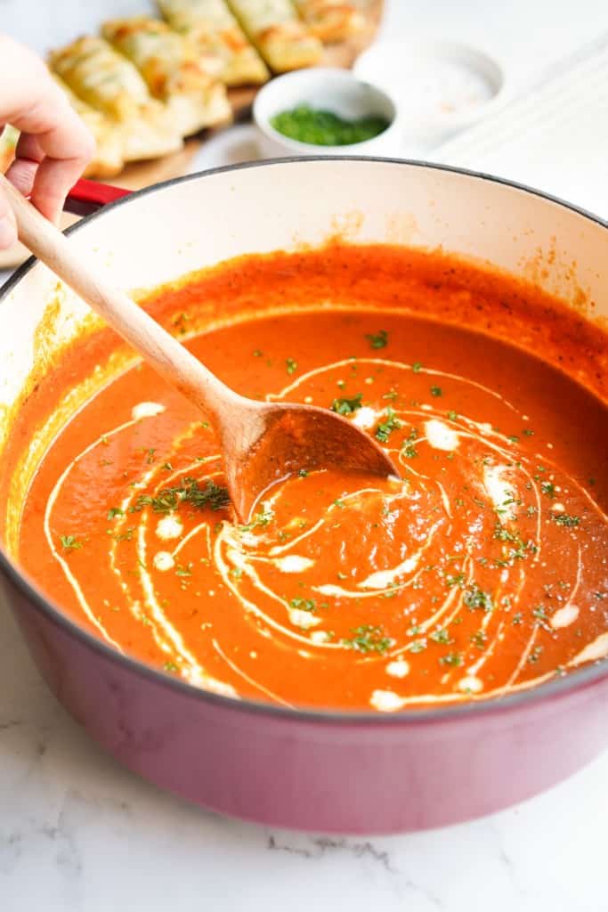 Using a wooden ladle to stir creamy roasted red pepper tomato soup