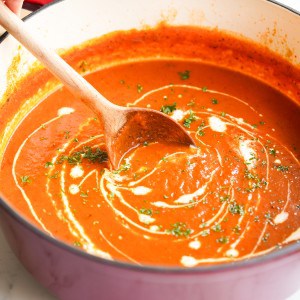 A Dutch oven filled with roasted red pepper and tomato soup, drizzled with heavy cream