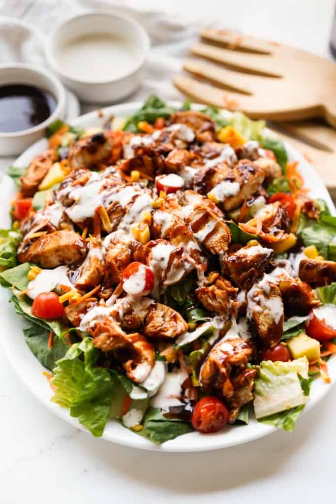 A large bed of lettuce topped with bbq chicken and drizzled with bbq sauce and ranch dressing