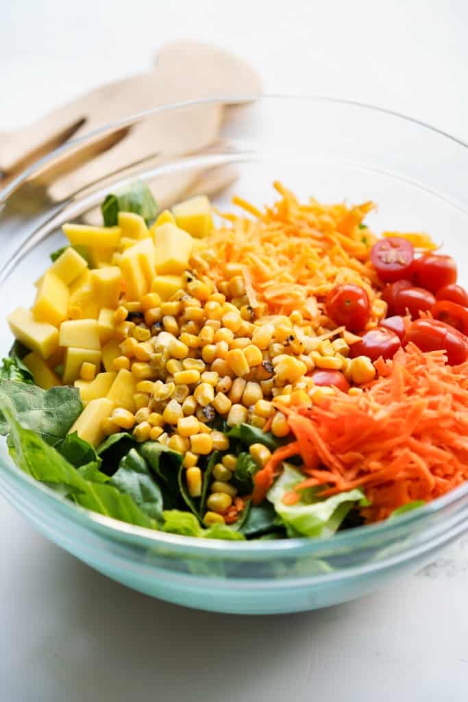 A bowl filled with green leaf lettuce, corn kernels, shredded carrots, halved cherry tomatoes and cheese