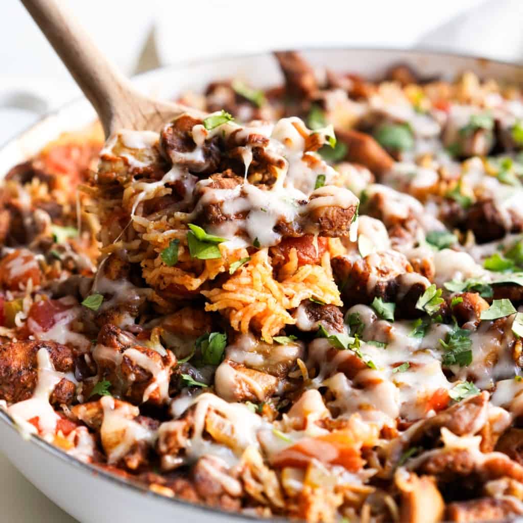 A wooden spatula scooping out Mexican rice with chicken topped with melted cheese and cilantro