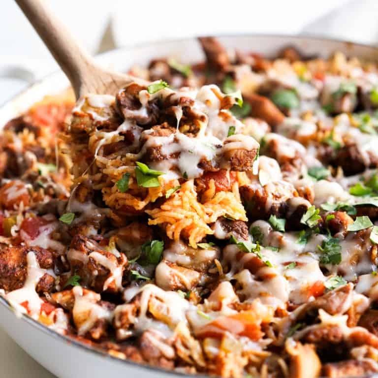 A wooden spatula scooping out Mexican rice with chicken topped with melted cheese and cilantro