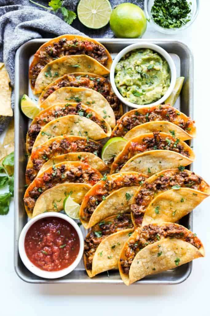 a platter of crispy beef tacos with guacamole and salsa