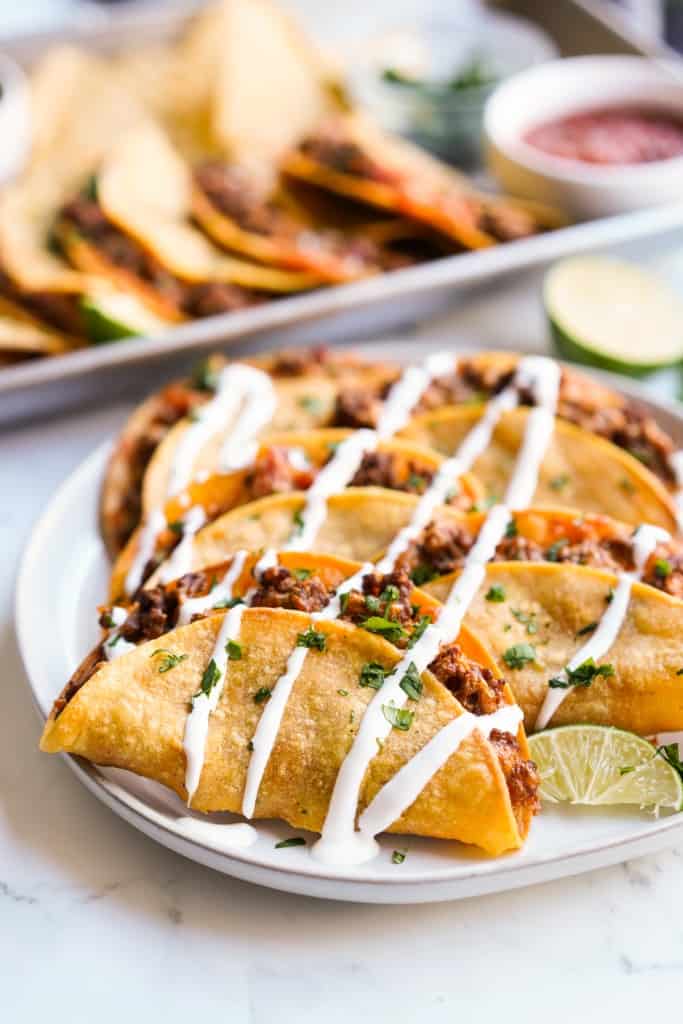 Baked ground beef tacos on a plate, drizzled with sour cream.