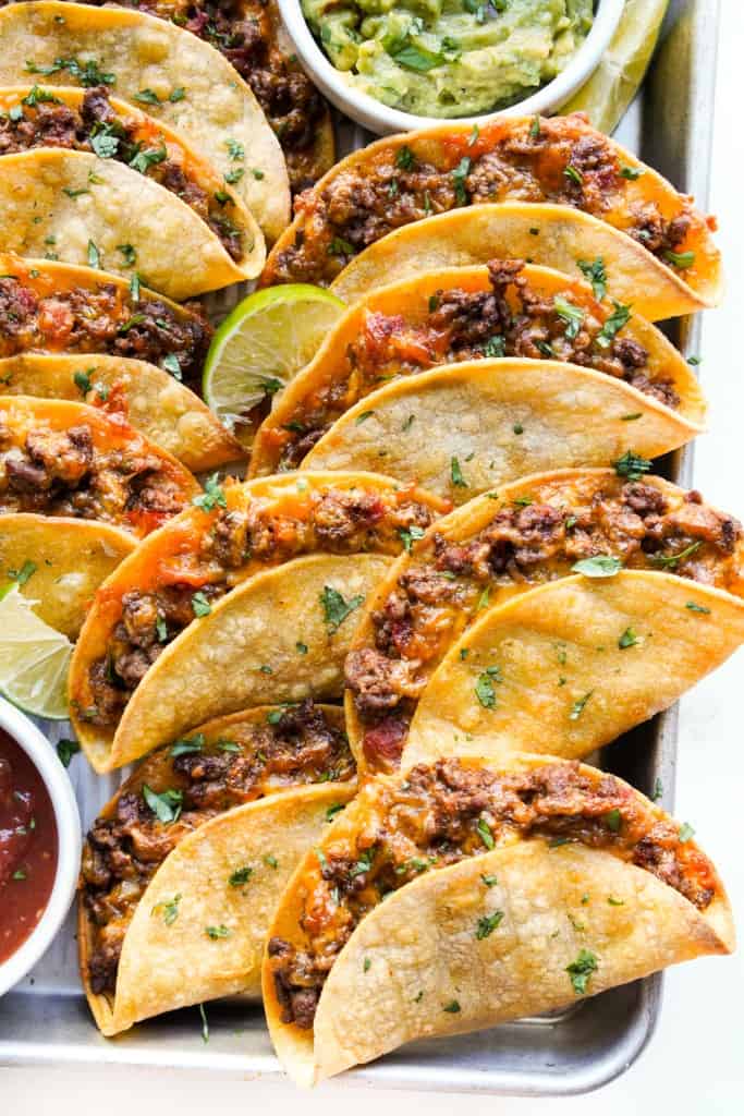 Crispy ground beef tacos piled on a sheet pan