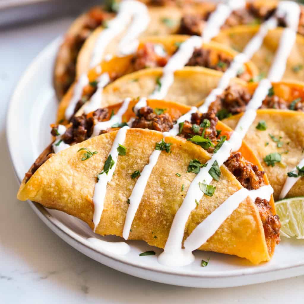 A plate of crispy beef tacos drizzled with sour cream.