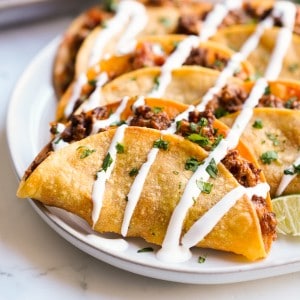 A plate of crispy beef tacos drizzled with sour cream.