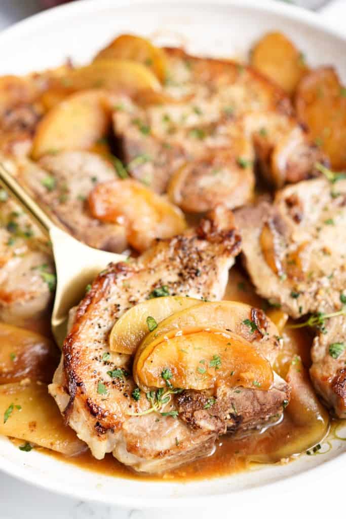 Lifting up a piece of bone-in pork chops topped with sliced cooked apples