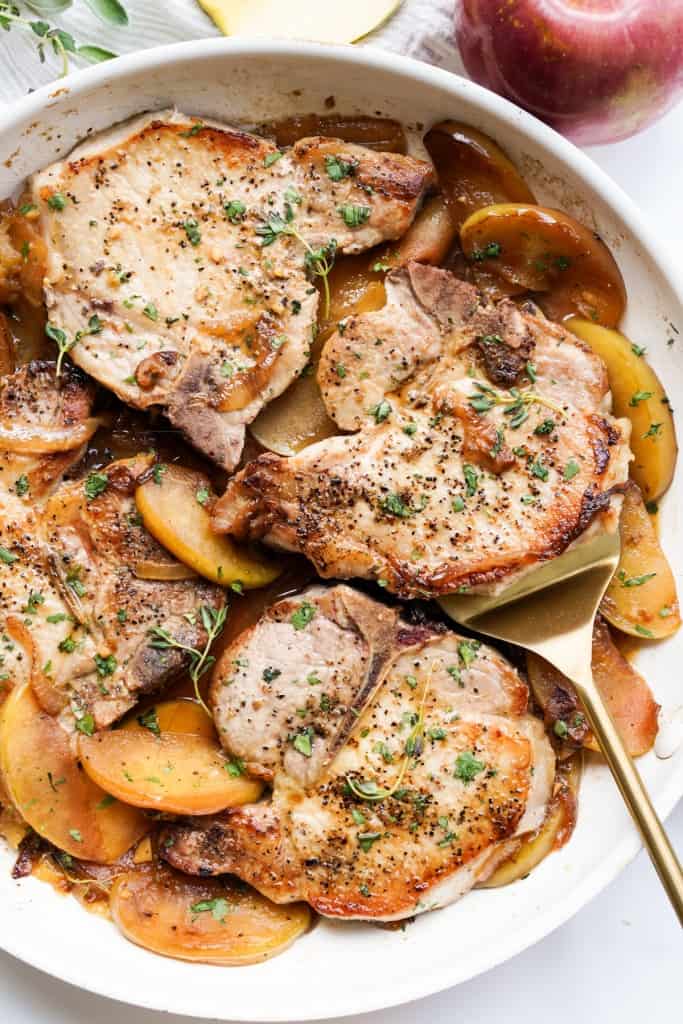 A skillet filled with pork chops and cooked apples and onions