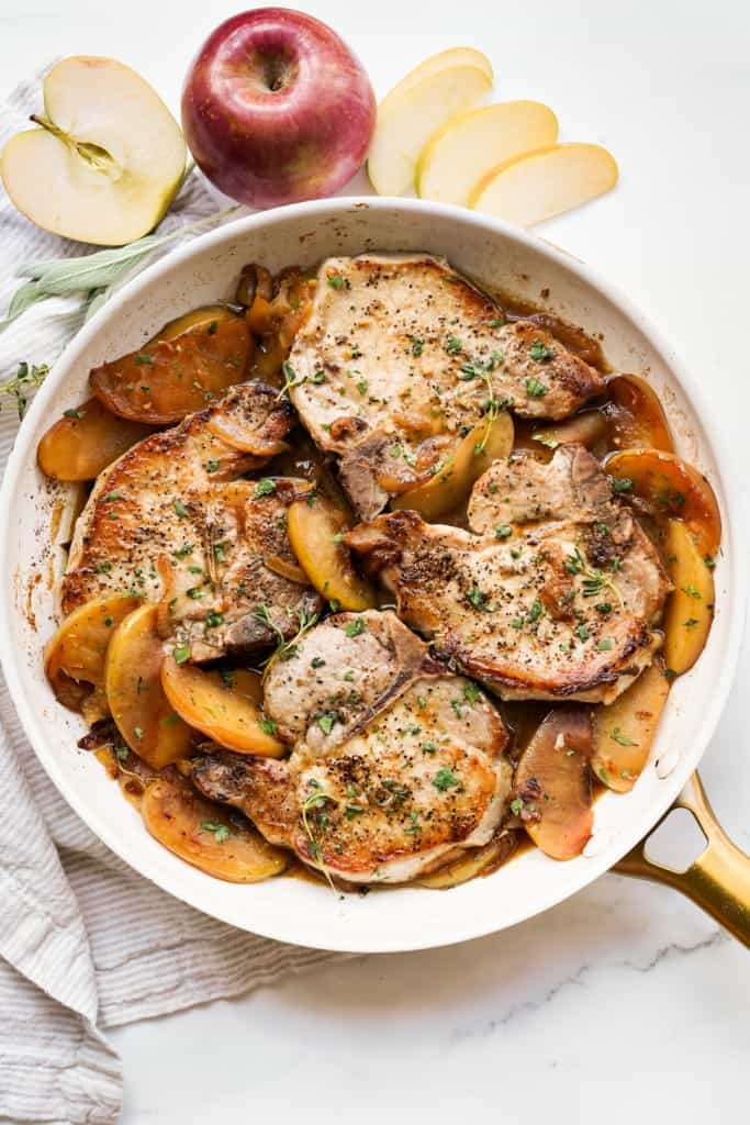 A large skillet of bone-in pork chops with apples and a little bit of juices
