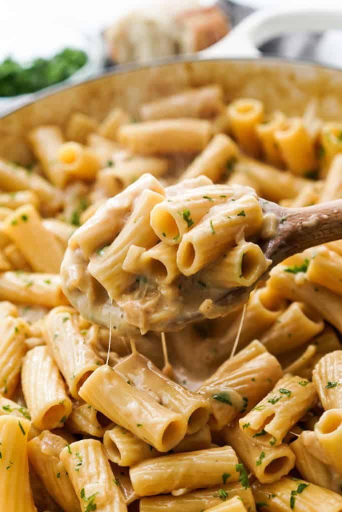 Scooping up creamy French onion pasta with a wooden spoon