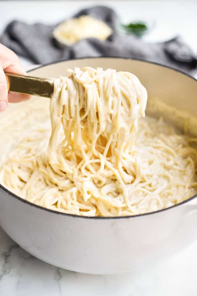 Lifting up spaghetti pasta coated in thick cheese sauce with a pair of tongs