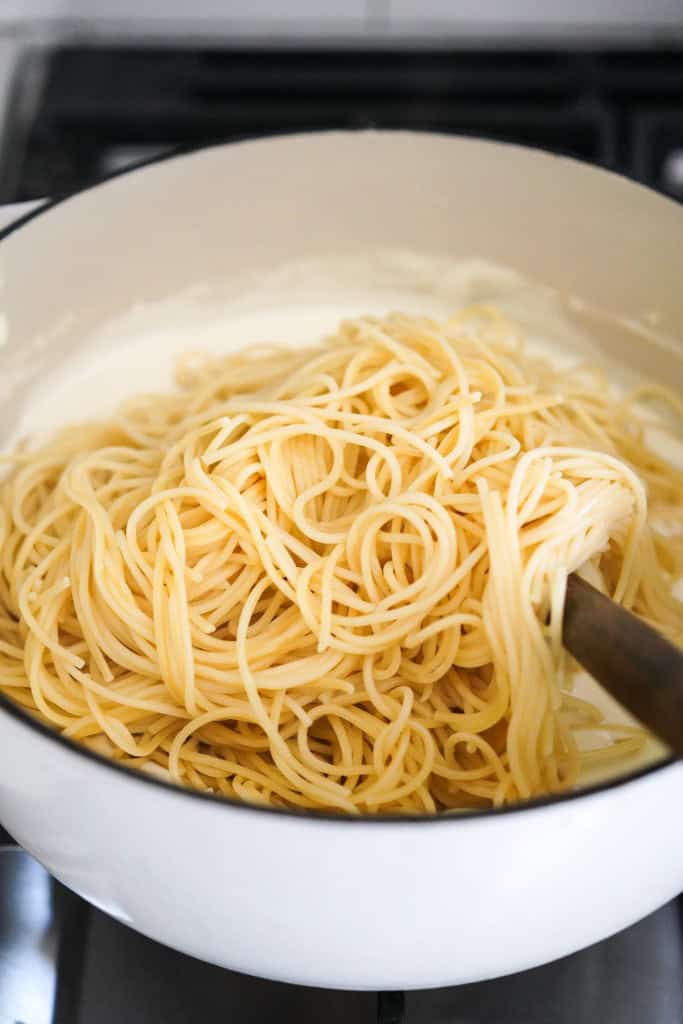 Spaghetti added to a pot of thick cheese sauce
