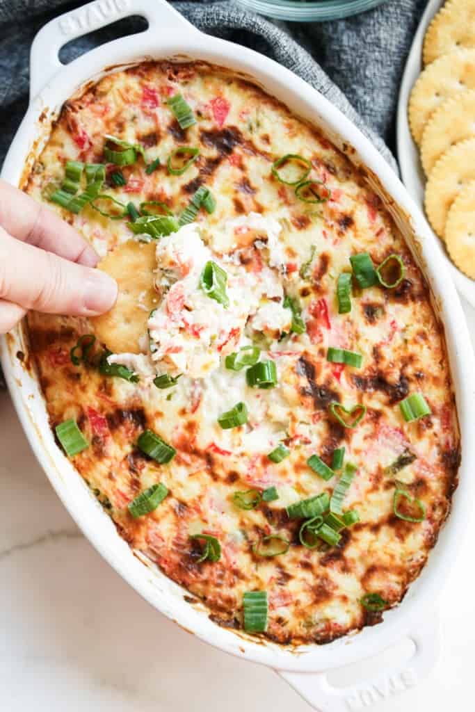 Dipping a cracker into an oval dish of crab rangoon dip