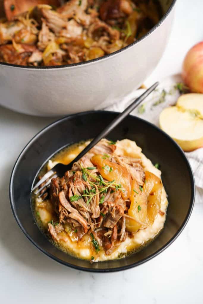 A bowl of braised pork with apples on top of mashed potatoes