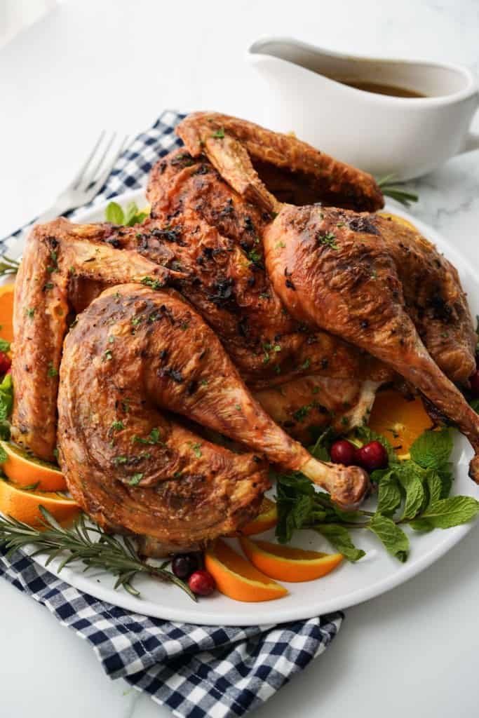 A whole turkey with crispy golden brown skin on a platter, with a gravy boat in the background