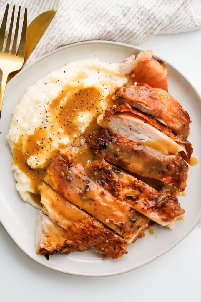 Sliced turkey breast with crispy skin on top of mashed potatoes with gravy