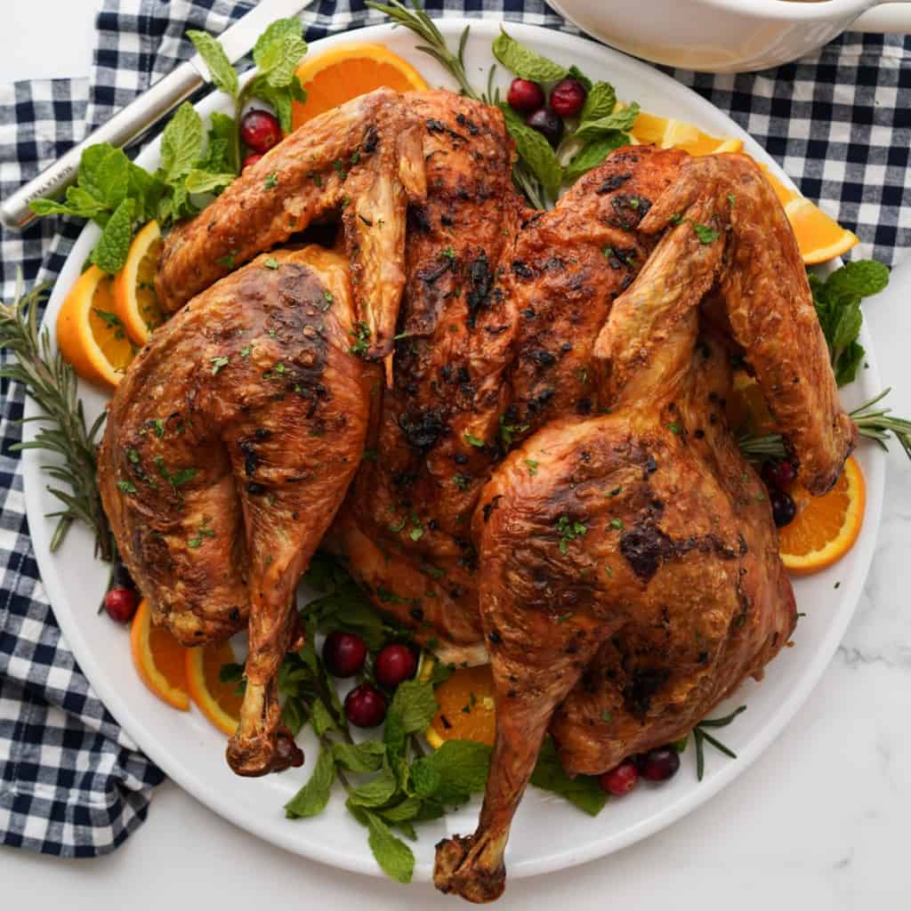 A spatchcock turkey on a platter, dressed with herbs, fresh cranberries and orange slices on the side