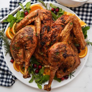 A spatchcock turkey on a platter, dressed with herbs, fresh cranberries and orange slices on the side