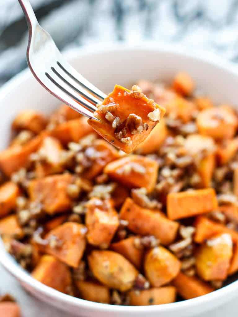 A fork picking up a piece of sticky caramelized sweet potato