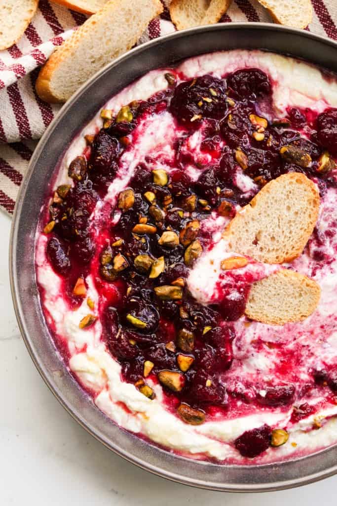 Baguette slices dipped into whipped feta topped with cranberry sauce and pistachios