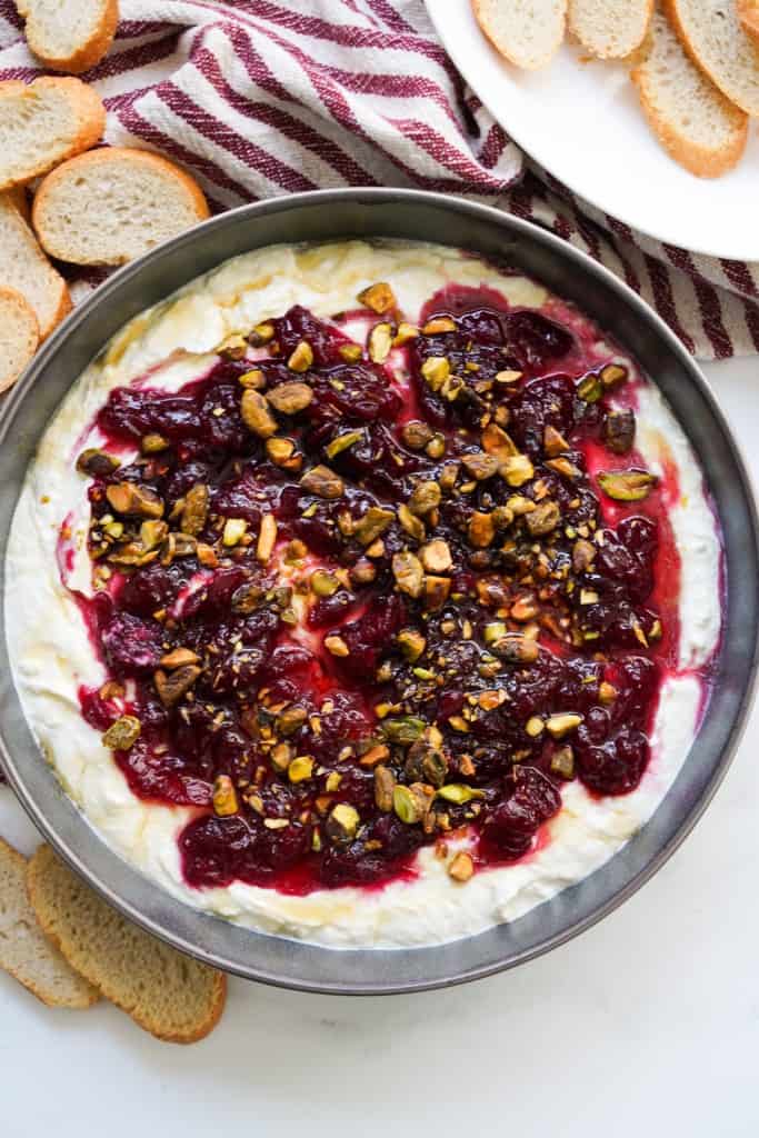 Top down view of a bowl of whipped feta with cranberry sauce, with crostini in the background