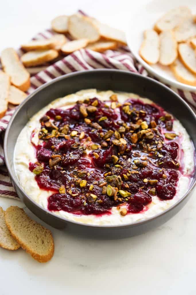 A shallow bowl of whipped feta topped with cranberry sauce, crushed pistachios, and drizzled with honey