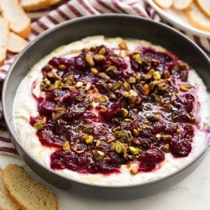 A bowl of cranberry whipped feta dip, with baguette slices in th background