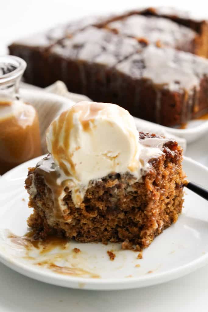A slice of sticky toffee pudding that has already been cut into, showing its moist cake texture