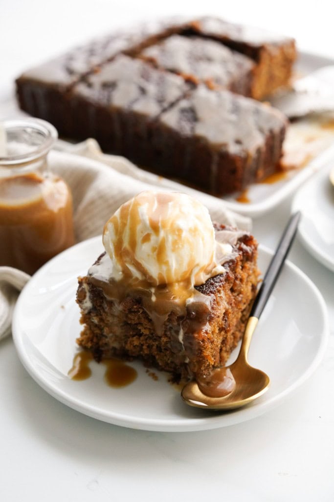 A slice of sticky toffee cake topped with toffee sauce and vanilla ice cream.