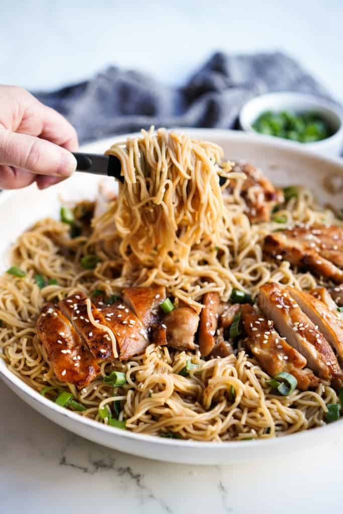 Picking up ramen noodles from a skillet filled with teriyaki noodles topped with chicken
