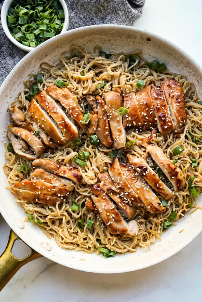 Top down view of a skillet loaded with teriyaki noodles topped with sliced teriyaki chicken