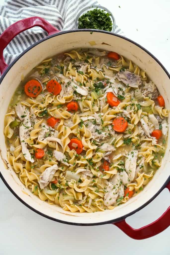 Top down view of a red Dutch oven filled with chicken noodle soup with carrots and celery