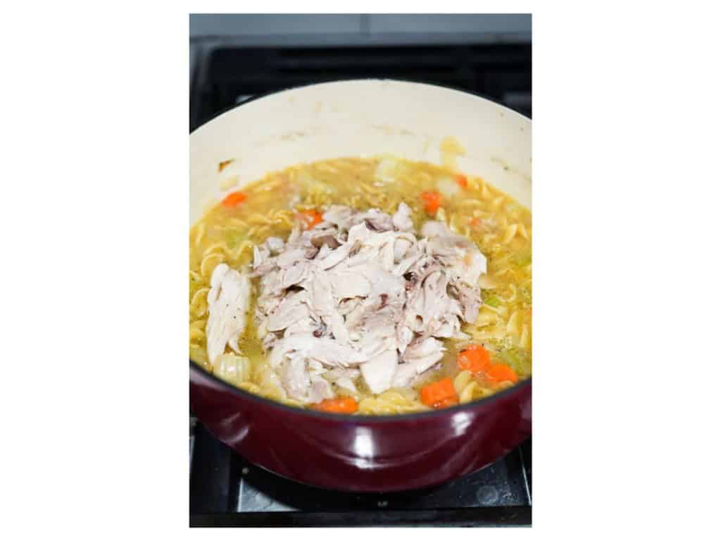Adding shredded chicken into a pot of noodles and broth