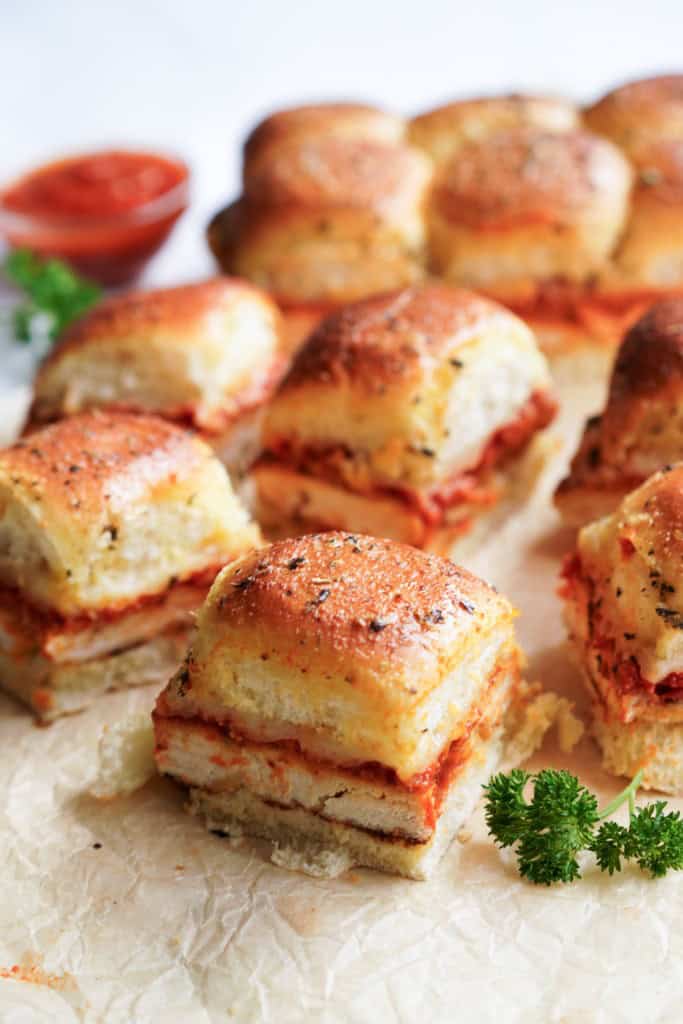 A close up picture of a parmesan chicken slider consisting of Hawaiian rolls, bread chicken breasts, marinara sauce, and mozzarella cheese.