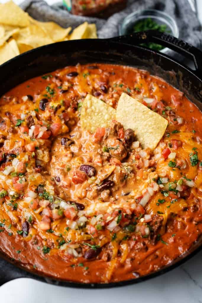 Two corn tortilla chips are dipped into a ground beef chili cheese dip.