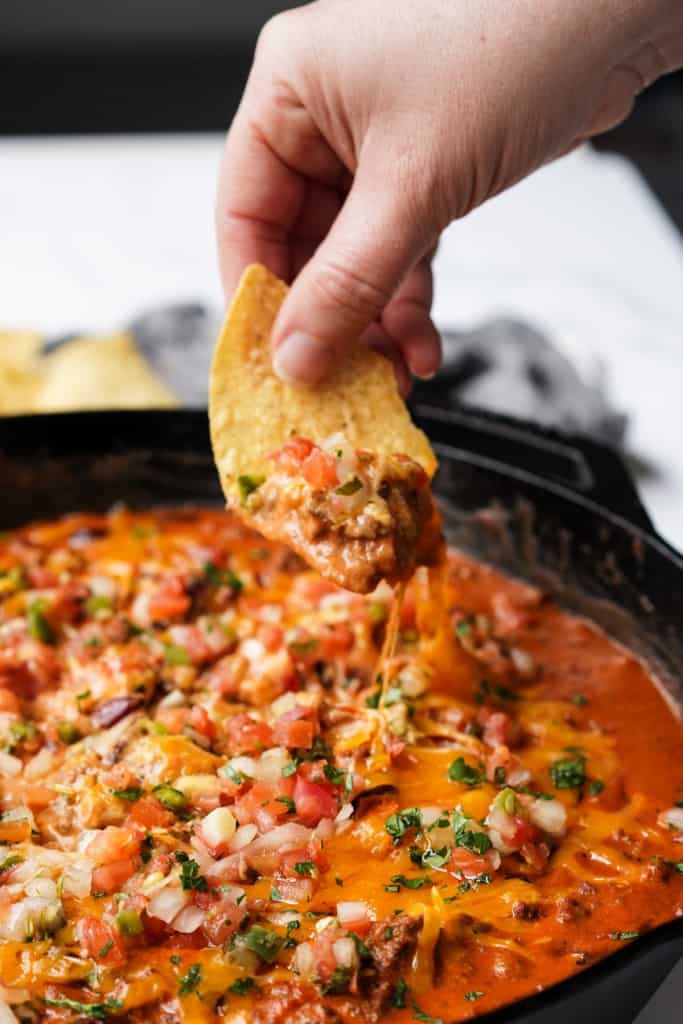 A corn tortilla chip has been dipped into chili cheese dip and lifted up.