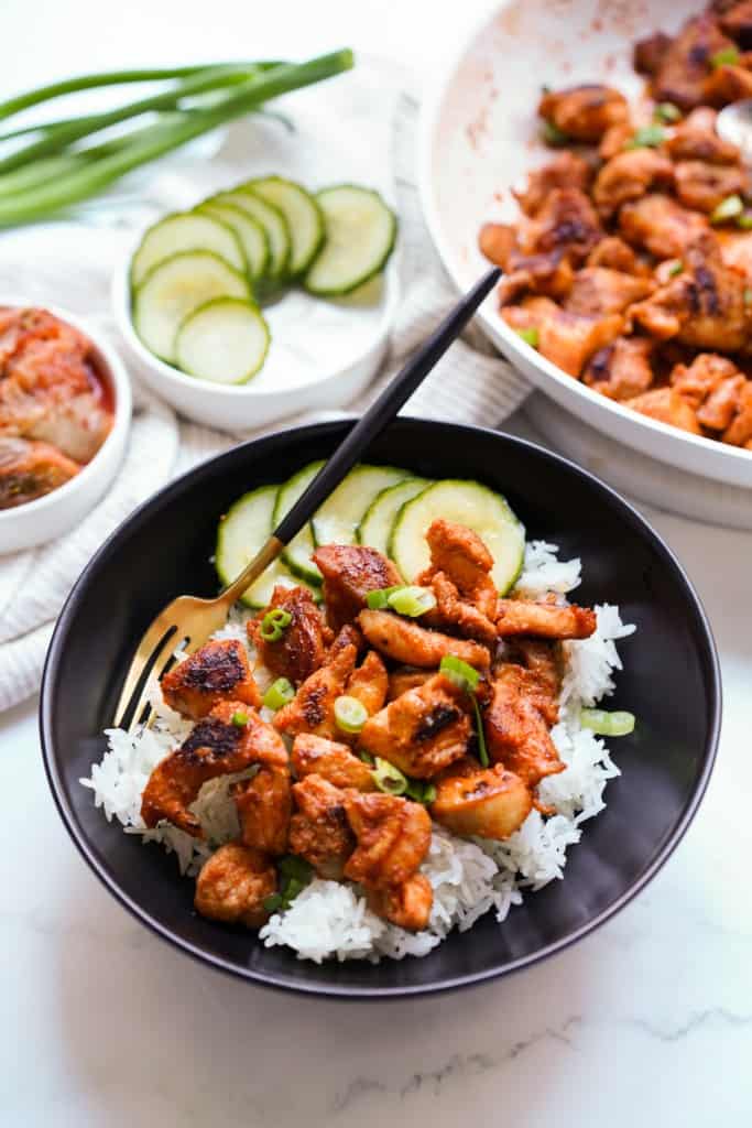 Gochujang chicken served on top of rice along with sliced cucumbers in a bowl