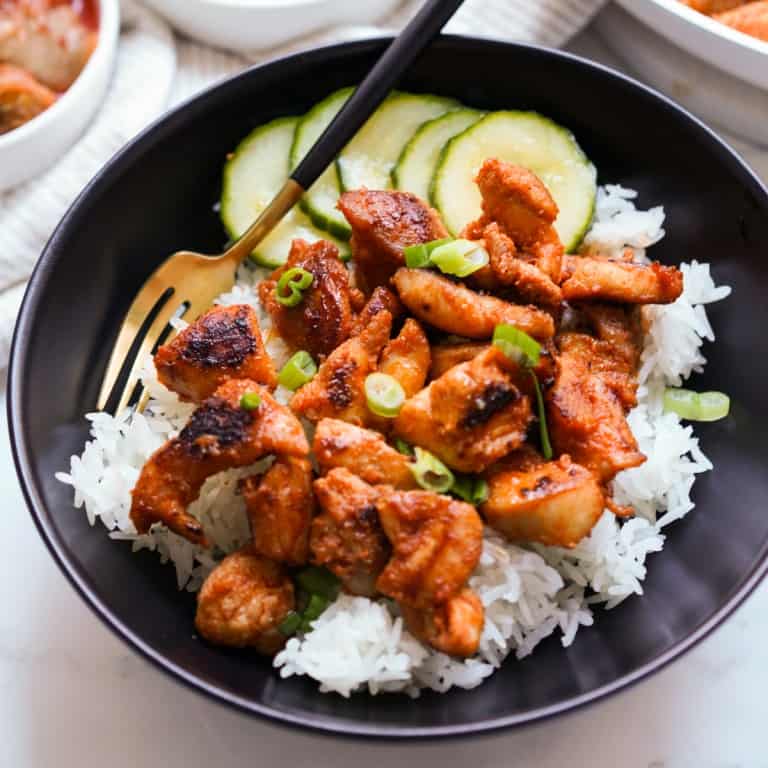 A bowl of rice topped with gochujang chicken and pickled cucumbers