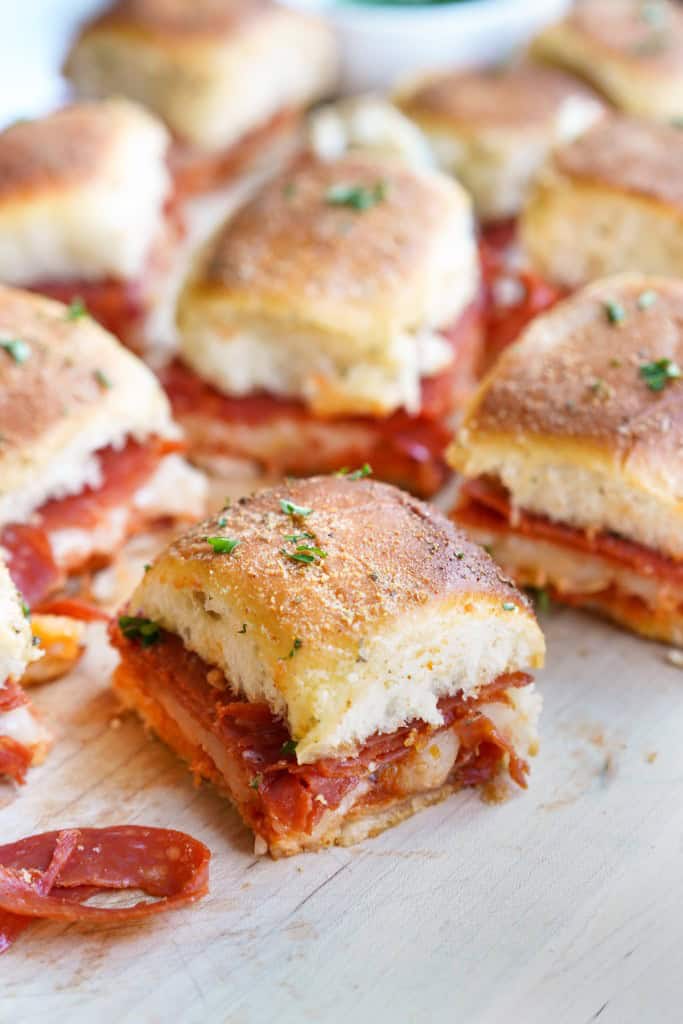 One pizza slider is in focus with several blurred in the background. The pepperoni is overflowing.
