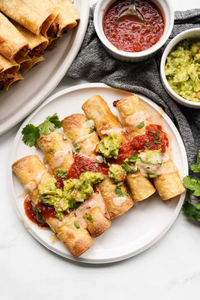 Top down view of cheese and chicken taquitos tipped with delicious sauces.