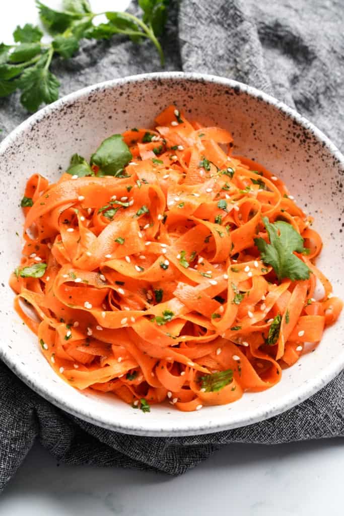 A bowl full of ribboned carrots topped with cilantro and sesame seeds.