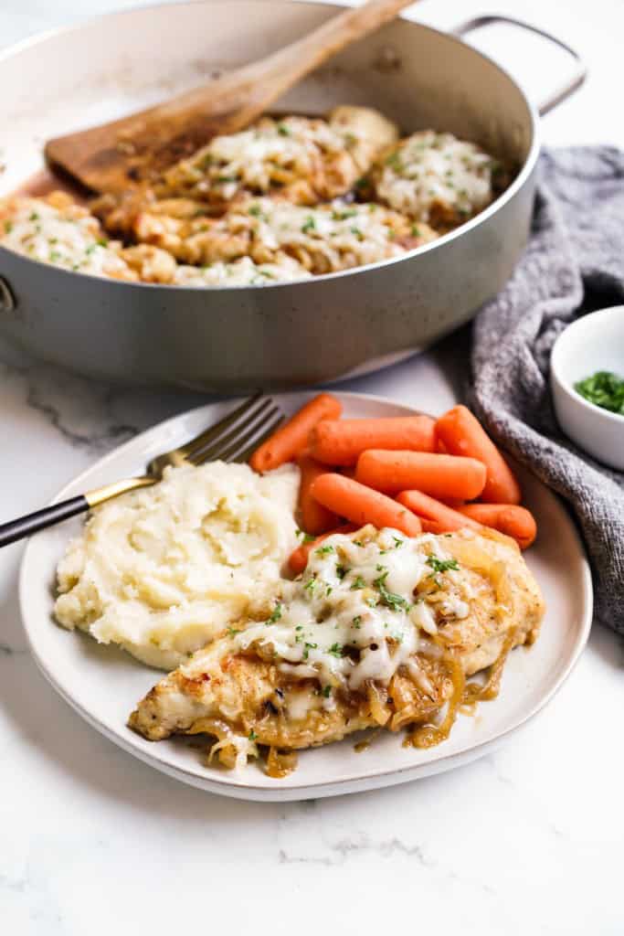 French Onion Chicken is plated with fluffy mashed potatoes and steamed baby carrots.