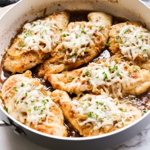 A close up shot of a deep sided skillet filled with french onion chicken breast, caramelized onions, and melted swiss cheese.