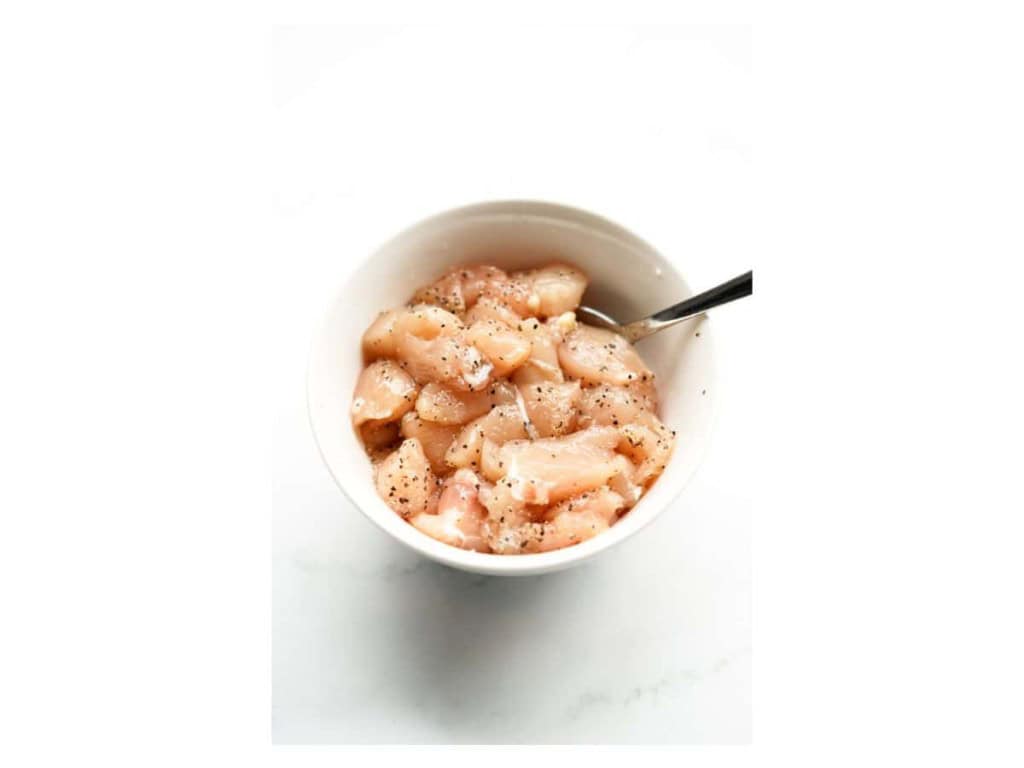 Small bowl filled with cubed chicken breat that has been seasoned with salt and pepper.