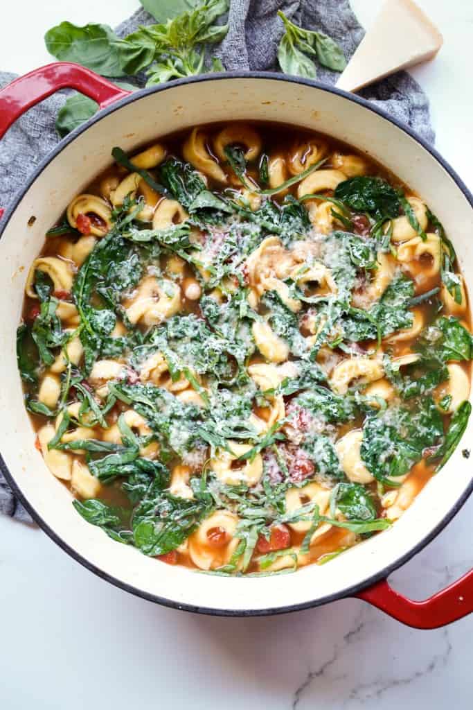 Top down picture of Spinach Tortellini Soup topped with grated parmesan cheese.